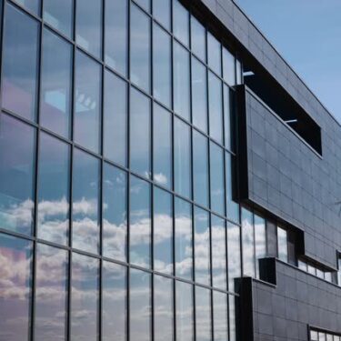 Clouds and sky are reflected in the glass windows of the facade of an office building. Stylish and strict architectural style of a commercial building. modern exterior
