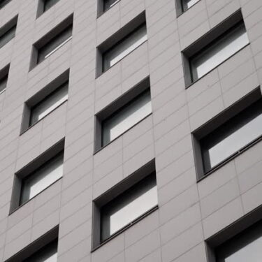 Modern high-rise building facade with repeating rectangular windows and minimalist geometric design elements captured from a diagonal perspective on a clear day.